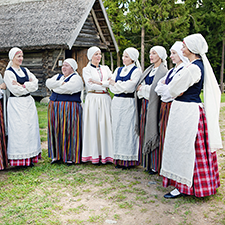 Latvian women are singing in the side by side in their traditional costumes.